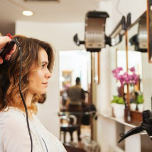 Hairdresser using curling tongs on customer's long brown hair in salon