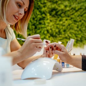 Happy beautician paint the nails of female clients at the beauty salon.